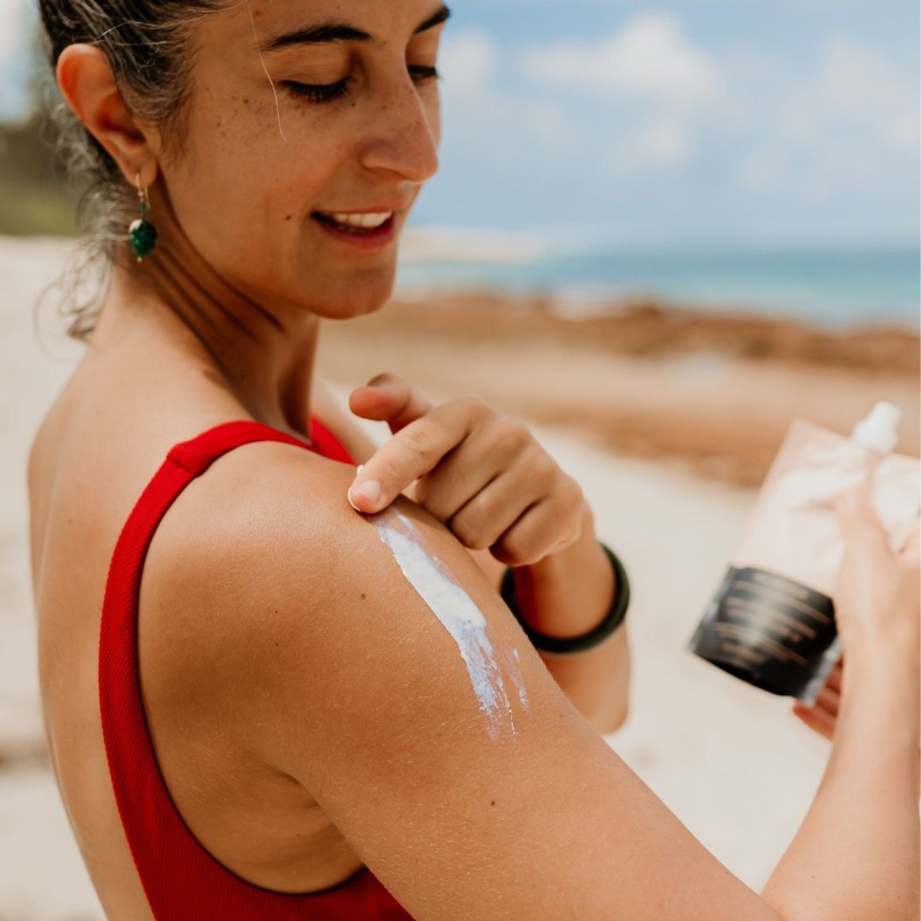 Sonnencreme wird am Meer auf die Schulter aufgetragen